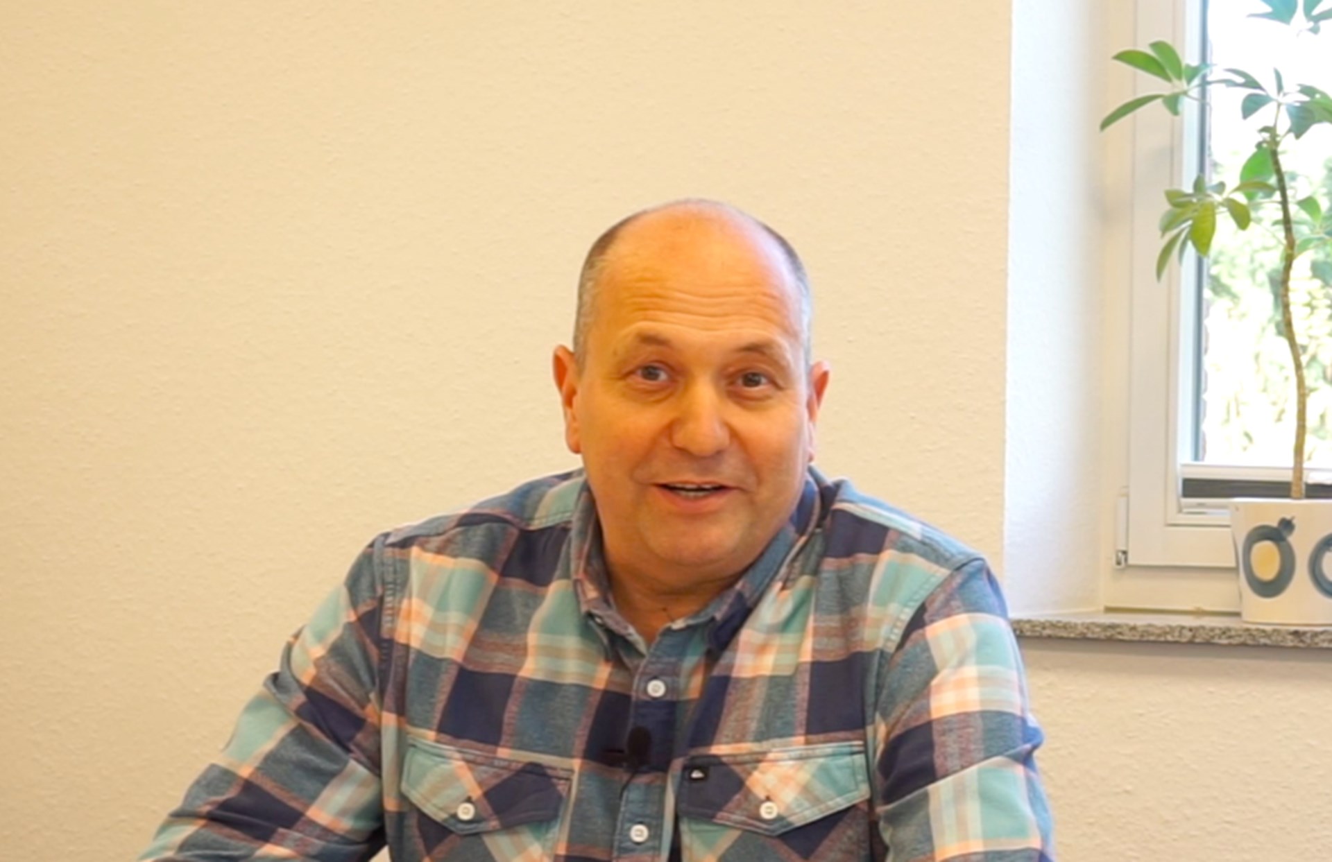 Gunnar Brock sitzt an einem Tisch, im Hintergrund ein Fenster mit Blumen auf der Fensterbank
