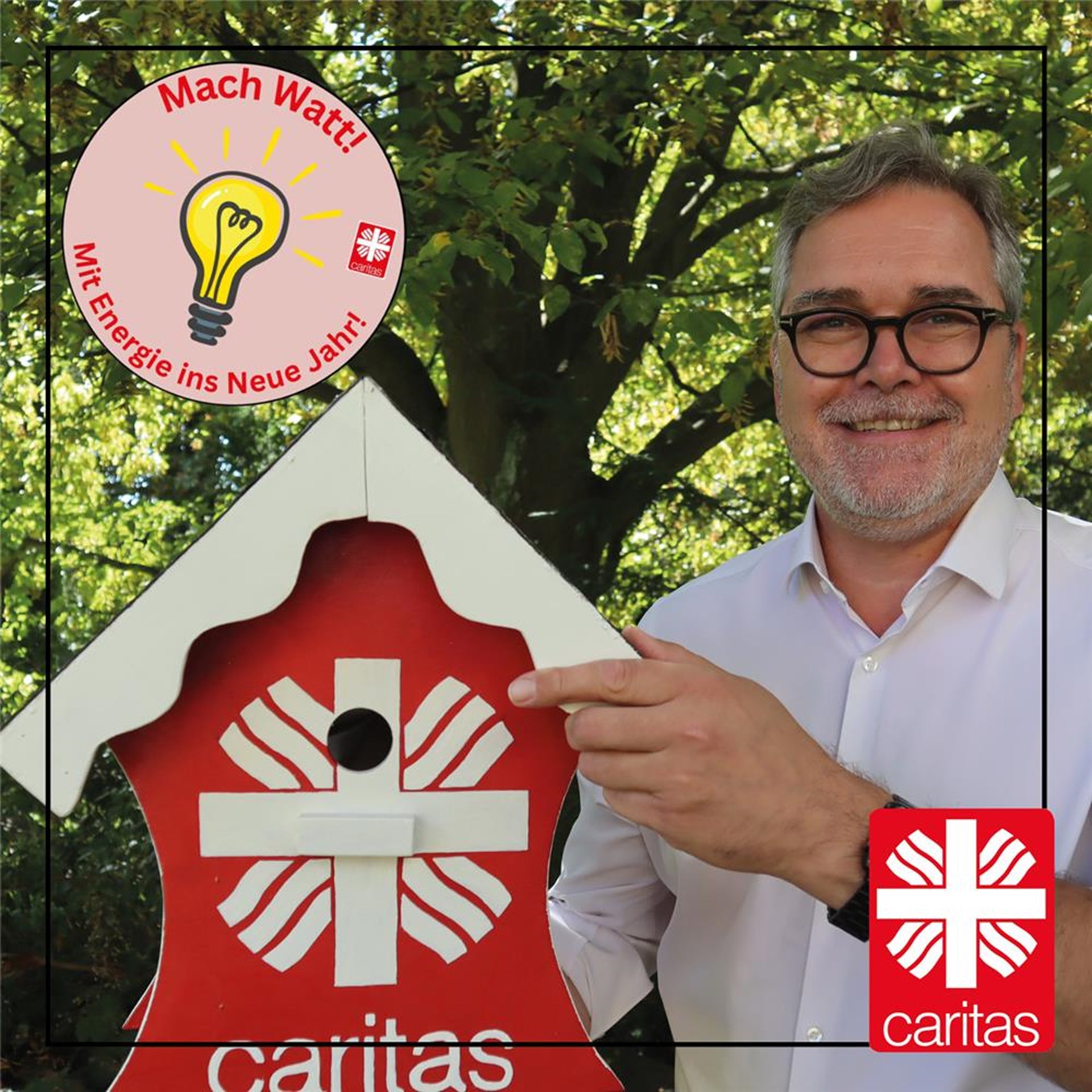 Mitarbeiter hält fröhlich rot-weißes Caritas-Vogelhaus in der Hand