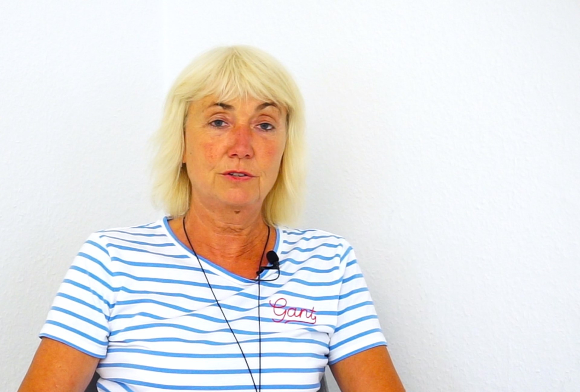 Ulrike Kamps sitzt vor einer weißen Wand und schaut in die Kamera