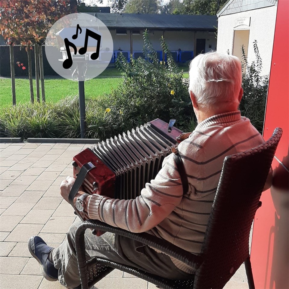 Senior sitzt mit einem Akkordeon auf dem Schoß draußen in der Herbstsonne 