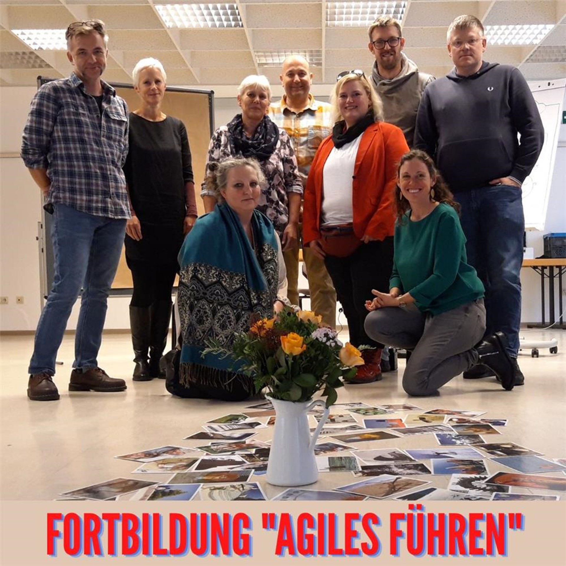 Auf dem Boden steht ein bunter Blumenstrauß, umgeben von kreativ-Fotokarten, dahinter stehen die Fortbildungsteilnehmenden