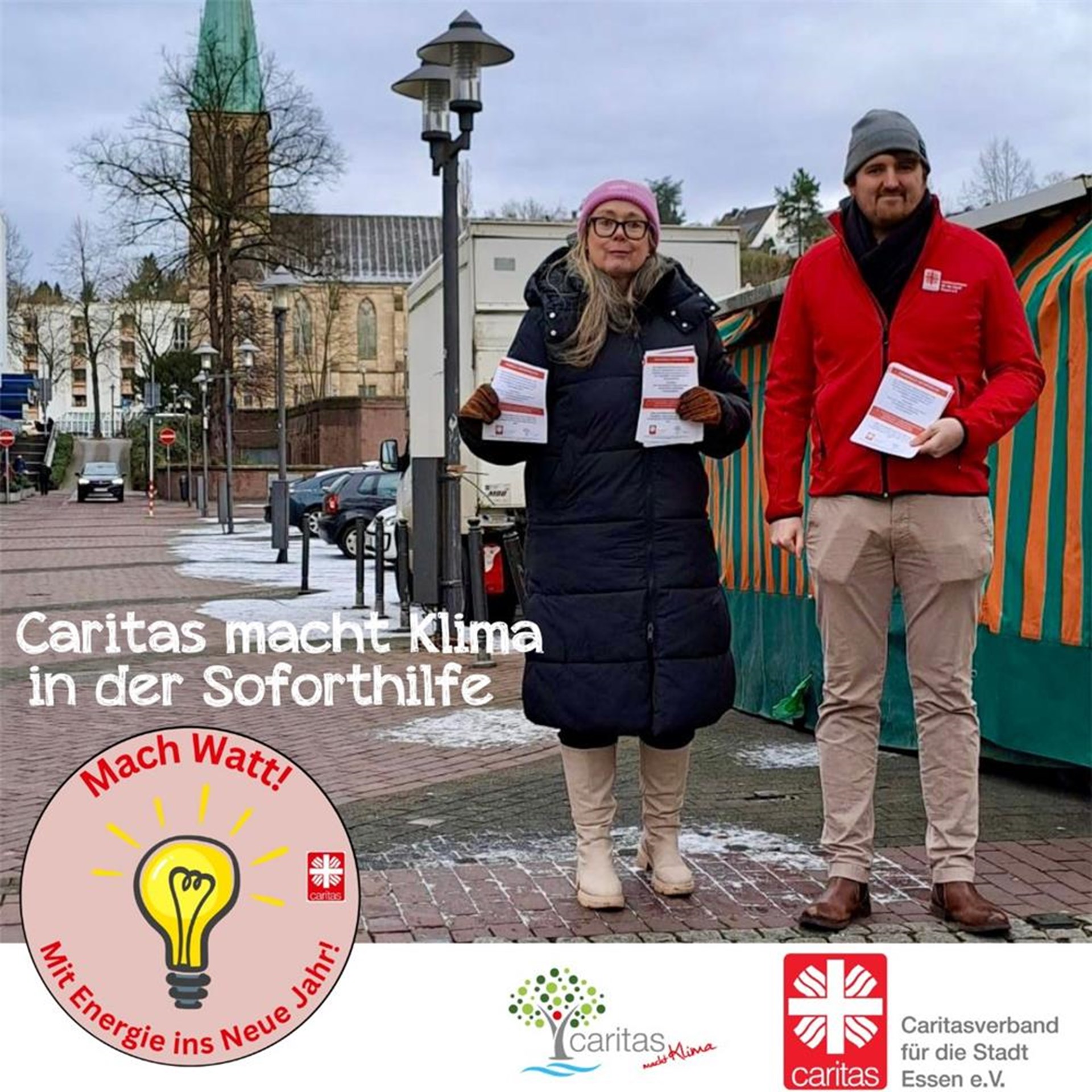 Die beiden Mitarbeitenden stehen, mit Infozetteln in der Hand, in der Fußgängerzone.