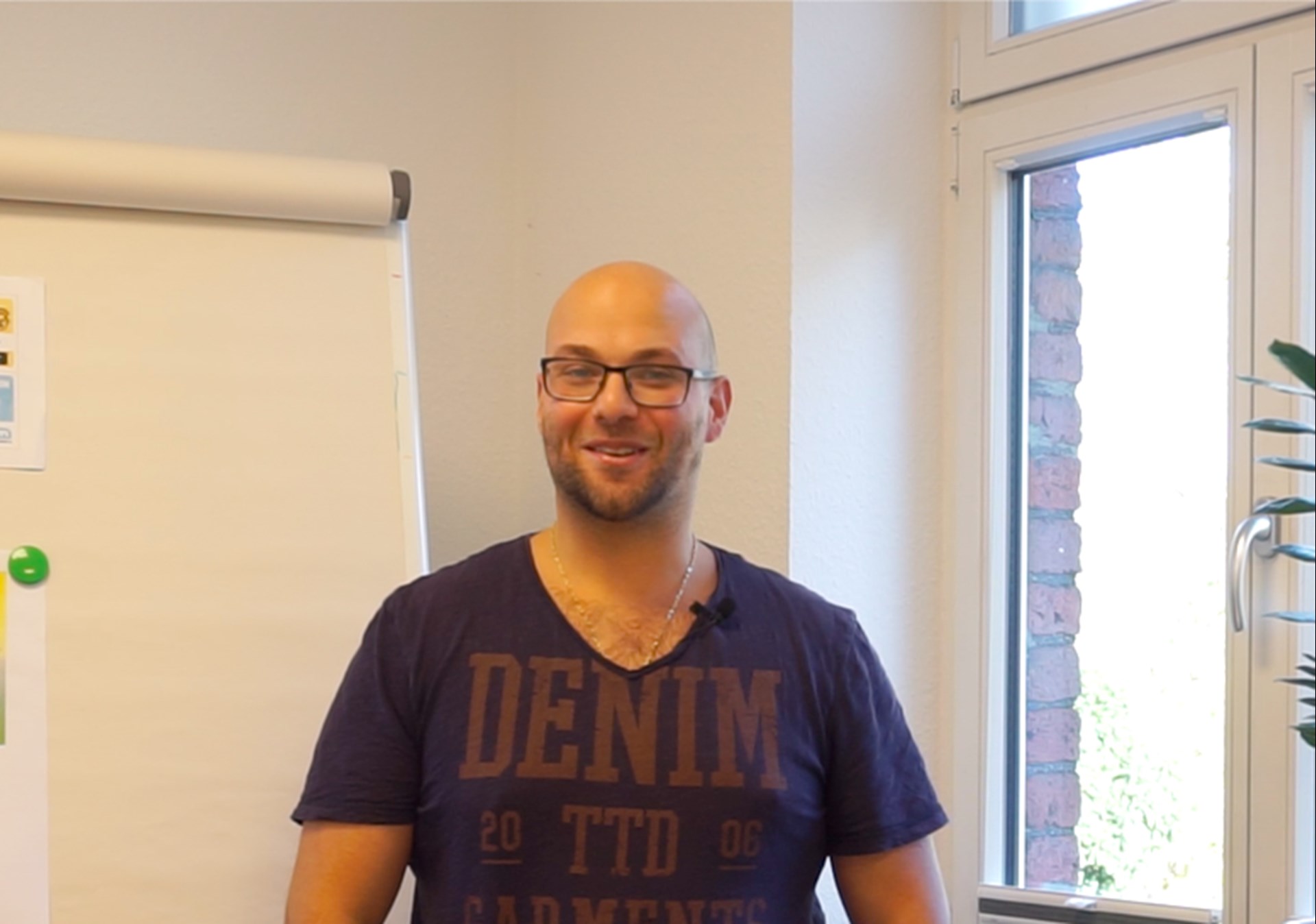 Carlo Marrone steht vor einem Flipchart und lächelt in die Kamera