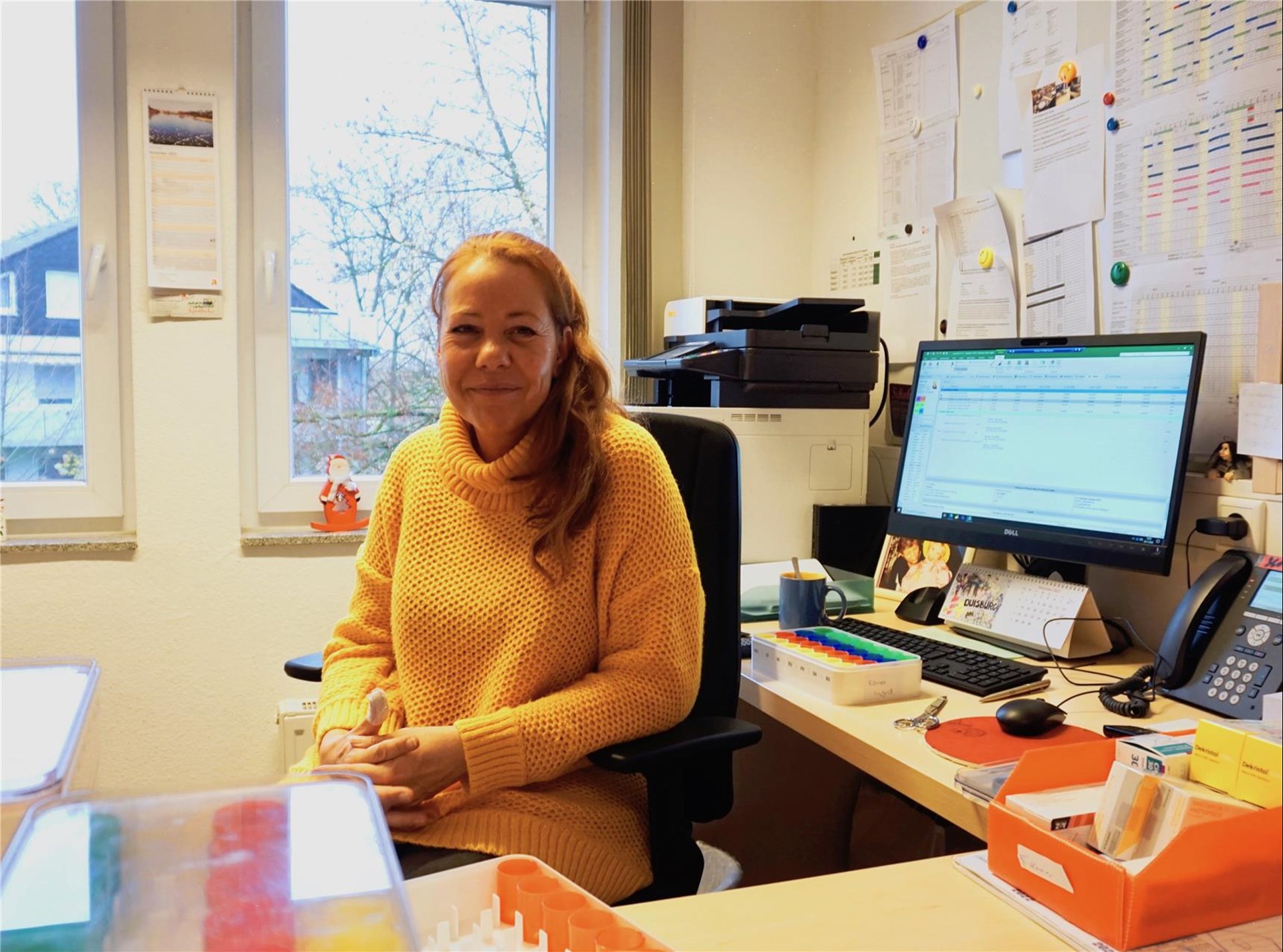 Claudia Witt sitzt an ihrem bunt gefüllten Schreibtisch und lächelt in die Kamera