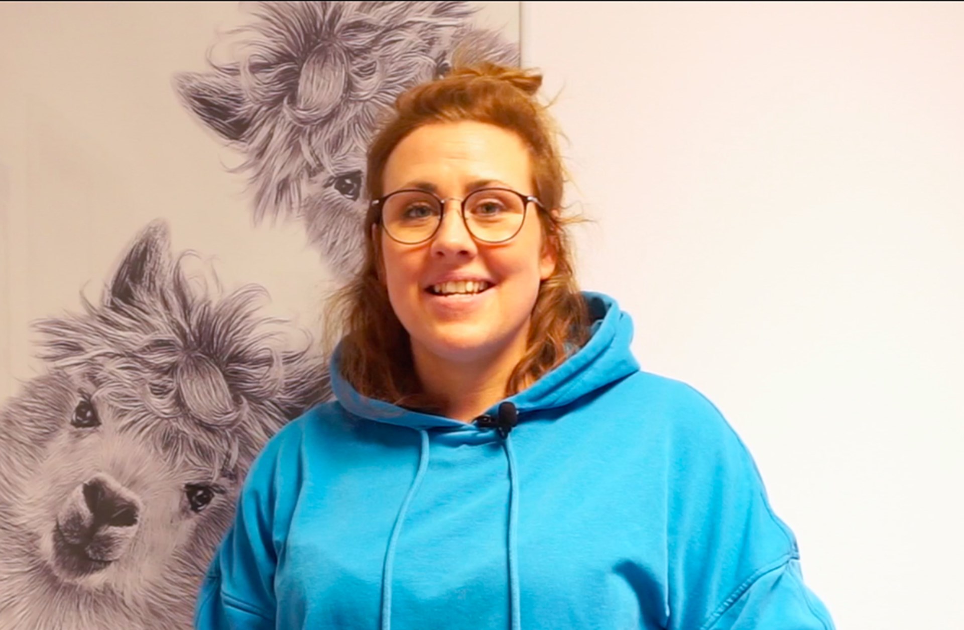 Svenja Sowa steht vor einem großen Bild mit Lamas und schaut in die Kamera