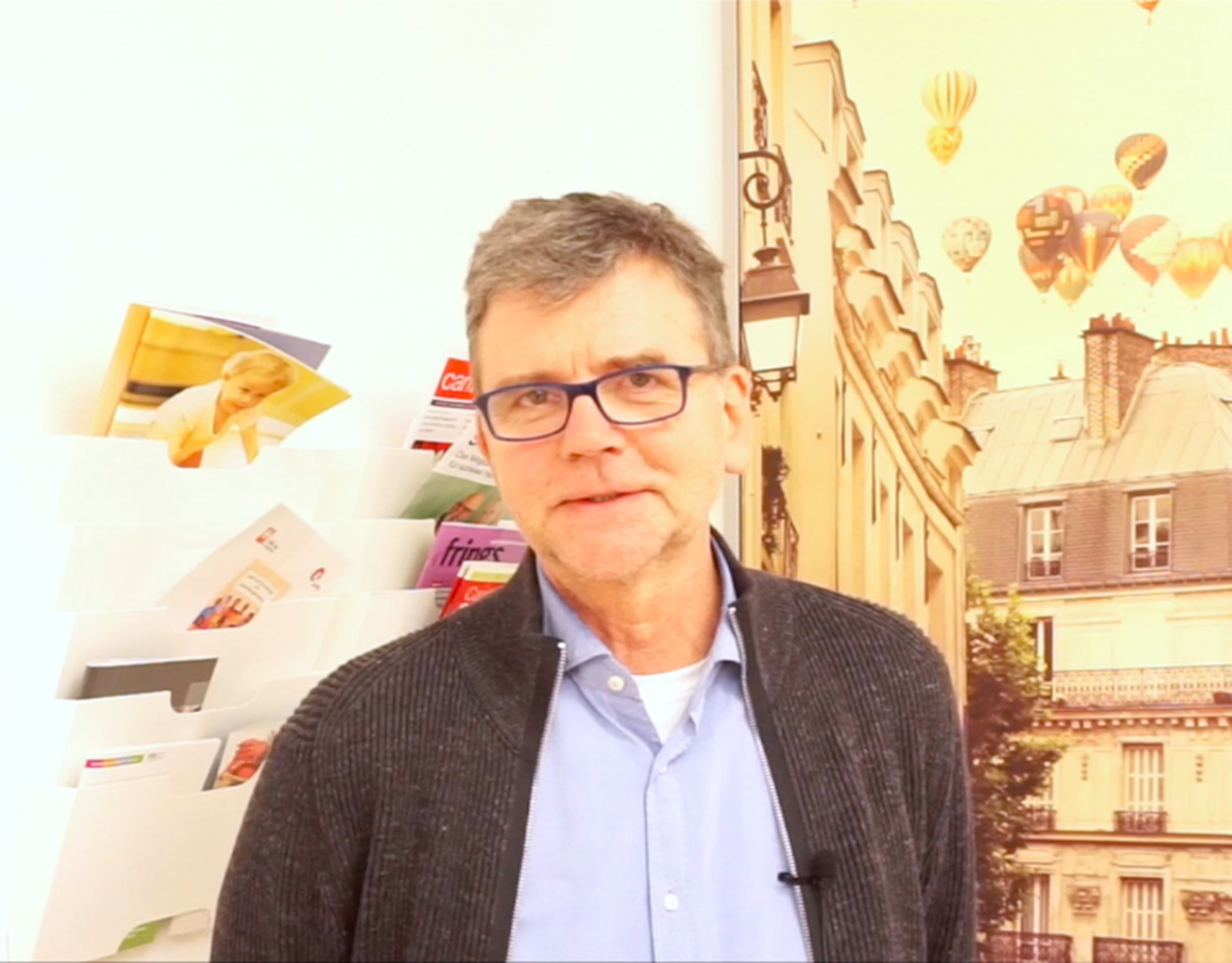 Ludger Thiesmeier steht vor einem bunten, großen Bild rechts und Magazinordnern an der Wand links